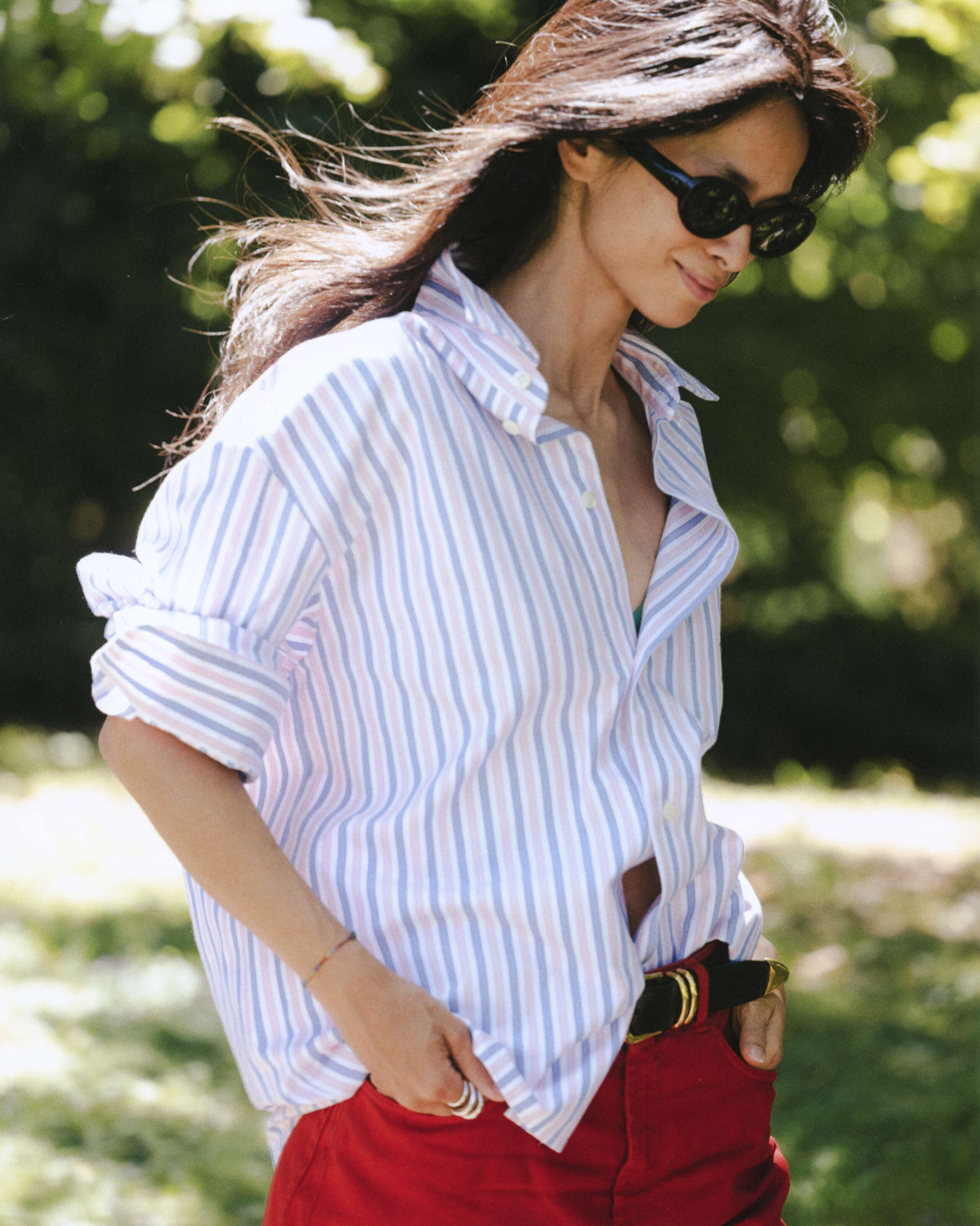 Picture of a women wearing a blouse featuring light blue and pink stripes and sunglasses