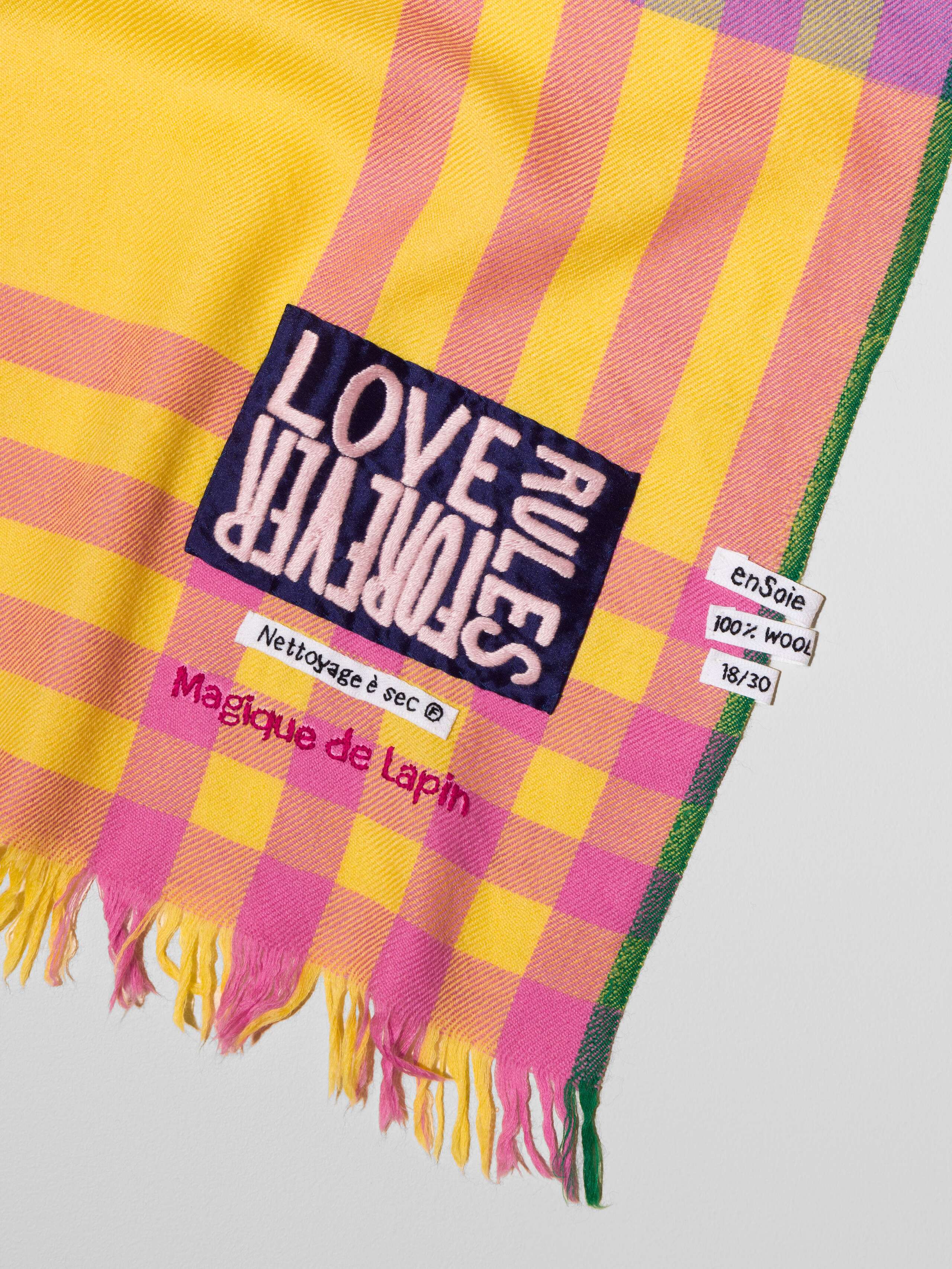 Picture of a detail of a wool scarf in a sunny yellow shade featuring a pink and lilac check pattern