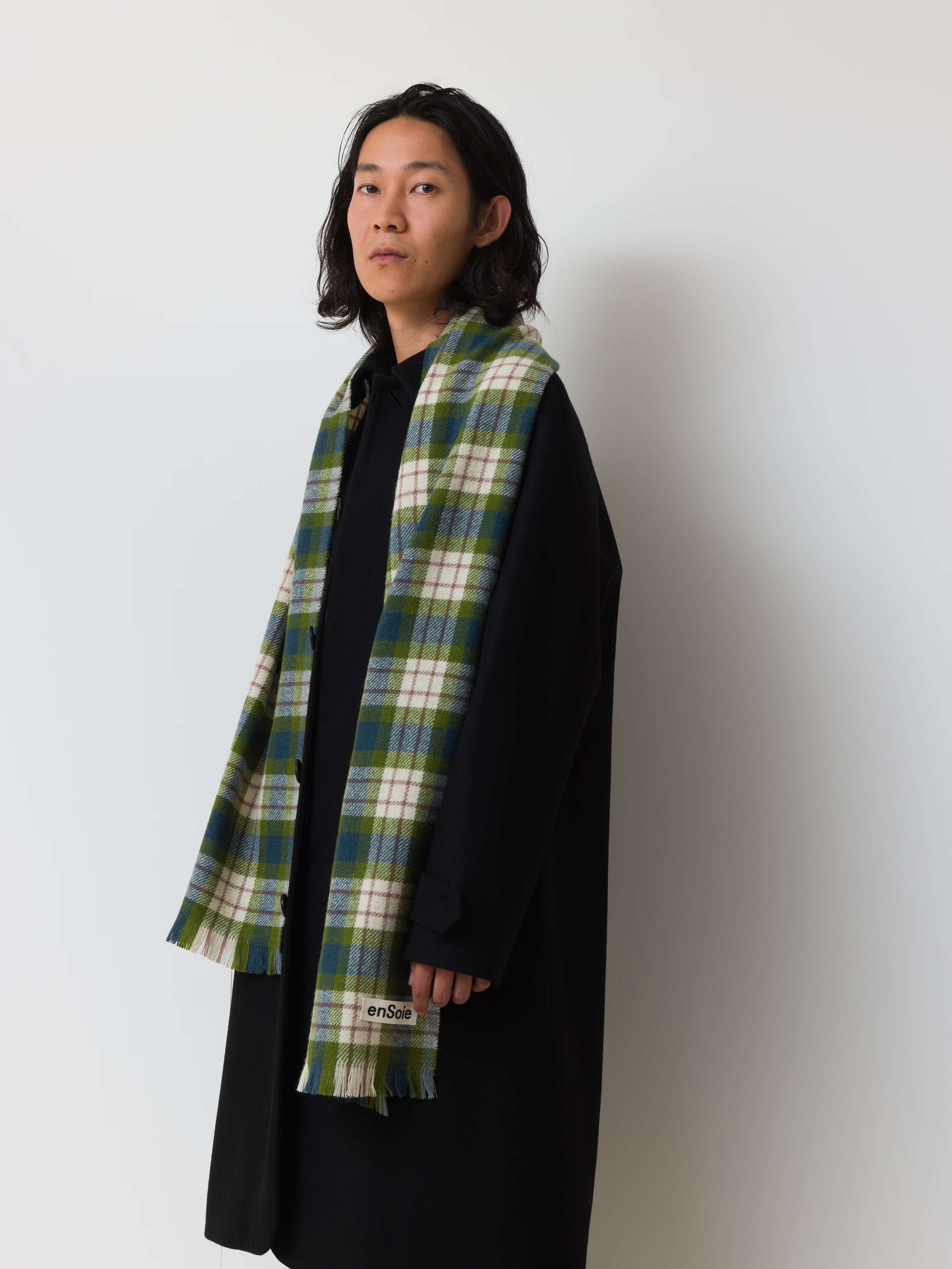 Picture of a male model wearing a black winter coat in combination with a greenish wool scarf