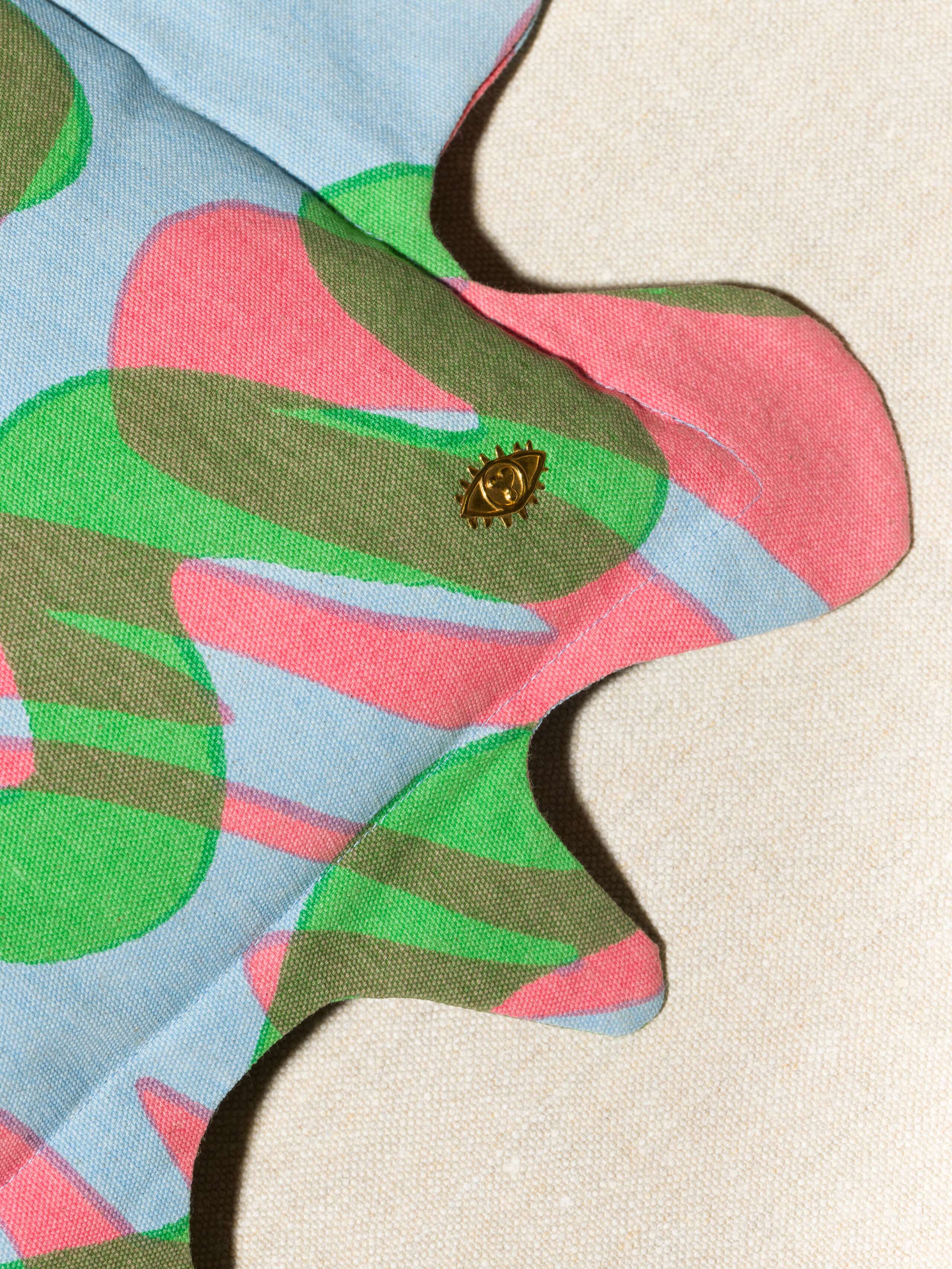 Picture of the wave print pillow cover with a wavy frame and brass eye detail in blue green pink pastels