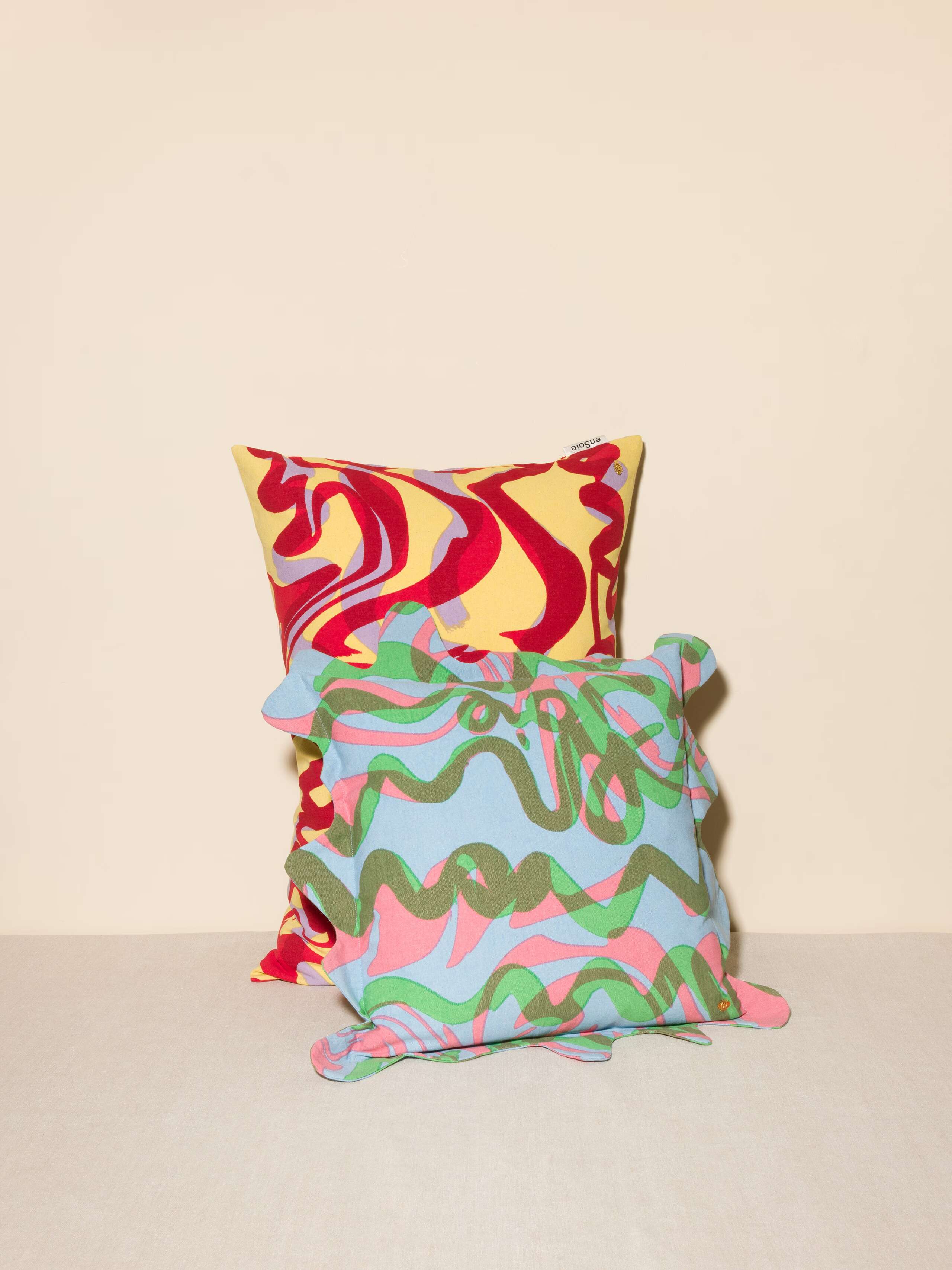 Picture of the wave print pillow cover with a wavy frame and brass eye detail in blue green pink pastels