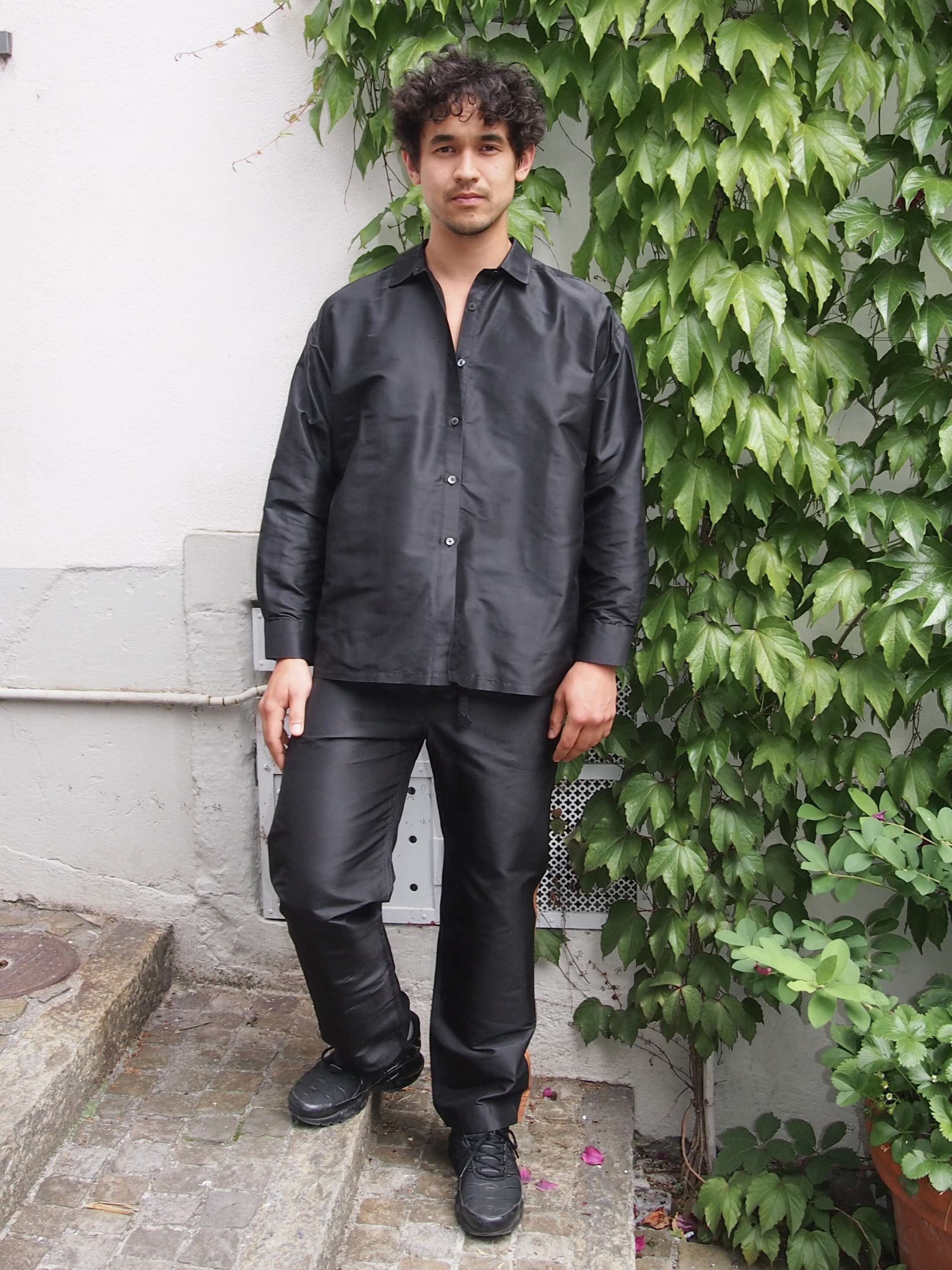 Picture of a male model wearing a black silk trousers in combination with a black silk shirt