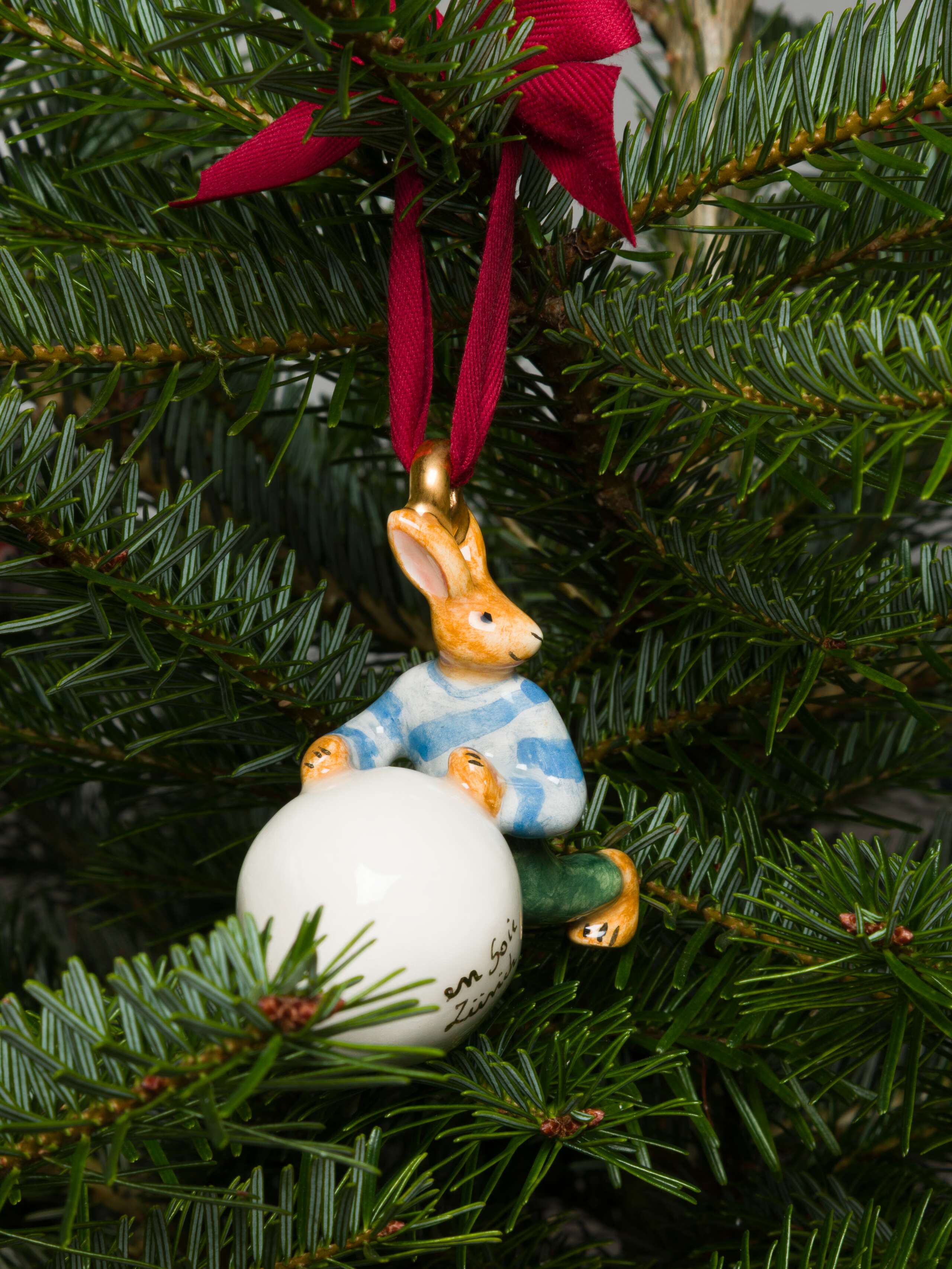 Rabbit rolling a snowball ceramic ornament on tree
