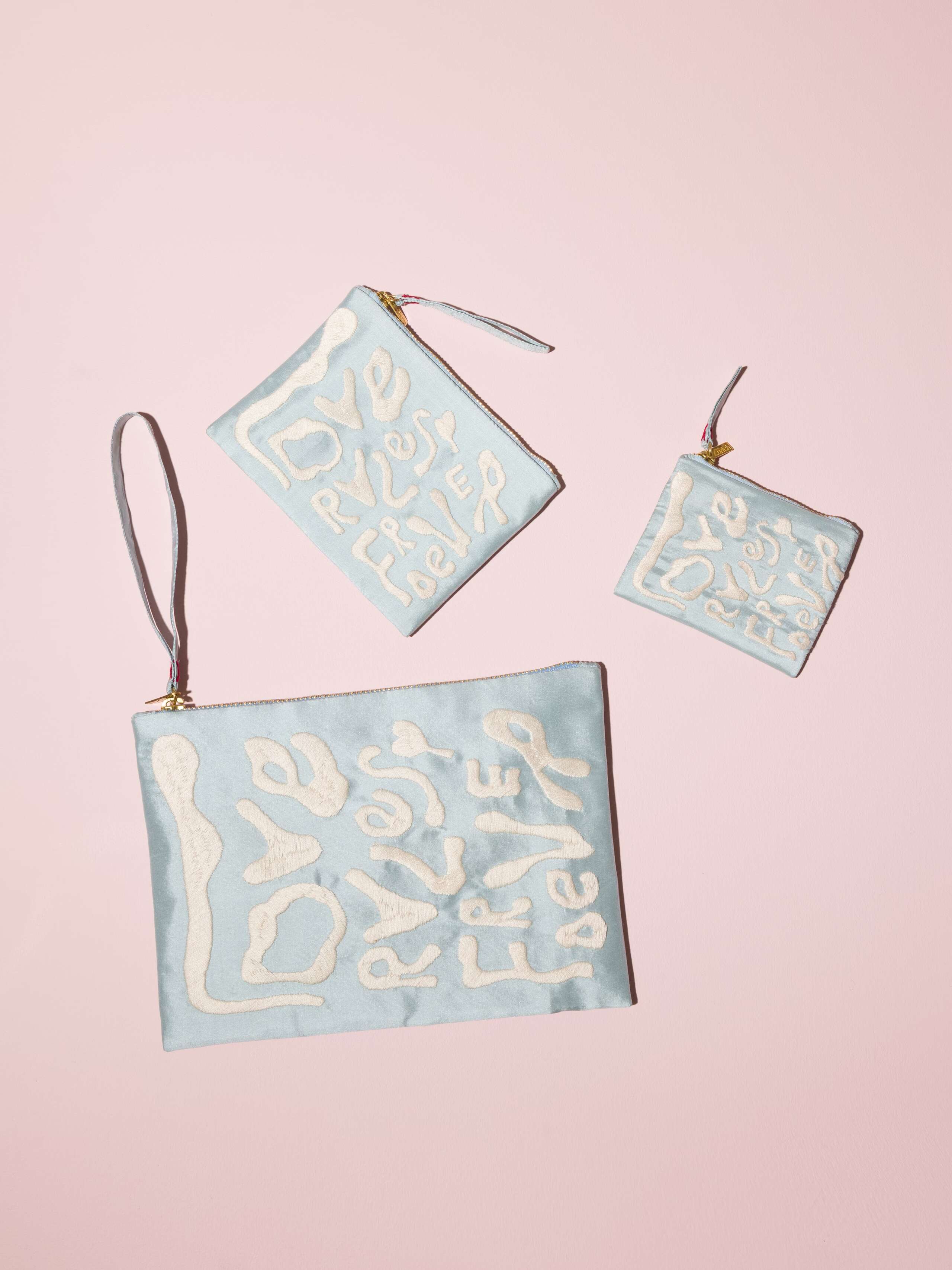 Picture of three light blue silk clutches featuring the motto Love Rules Forever