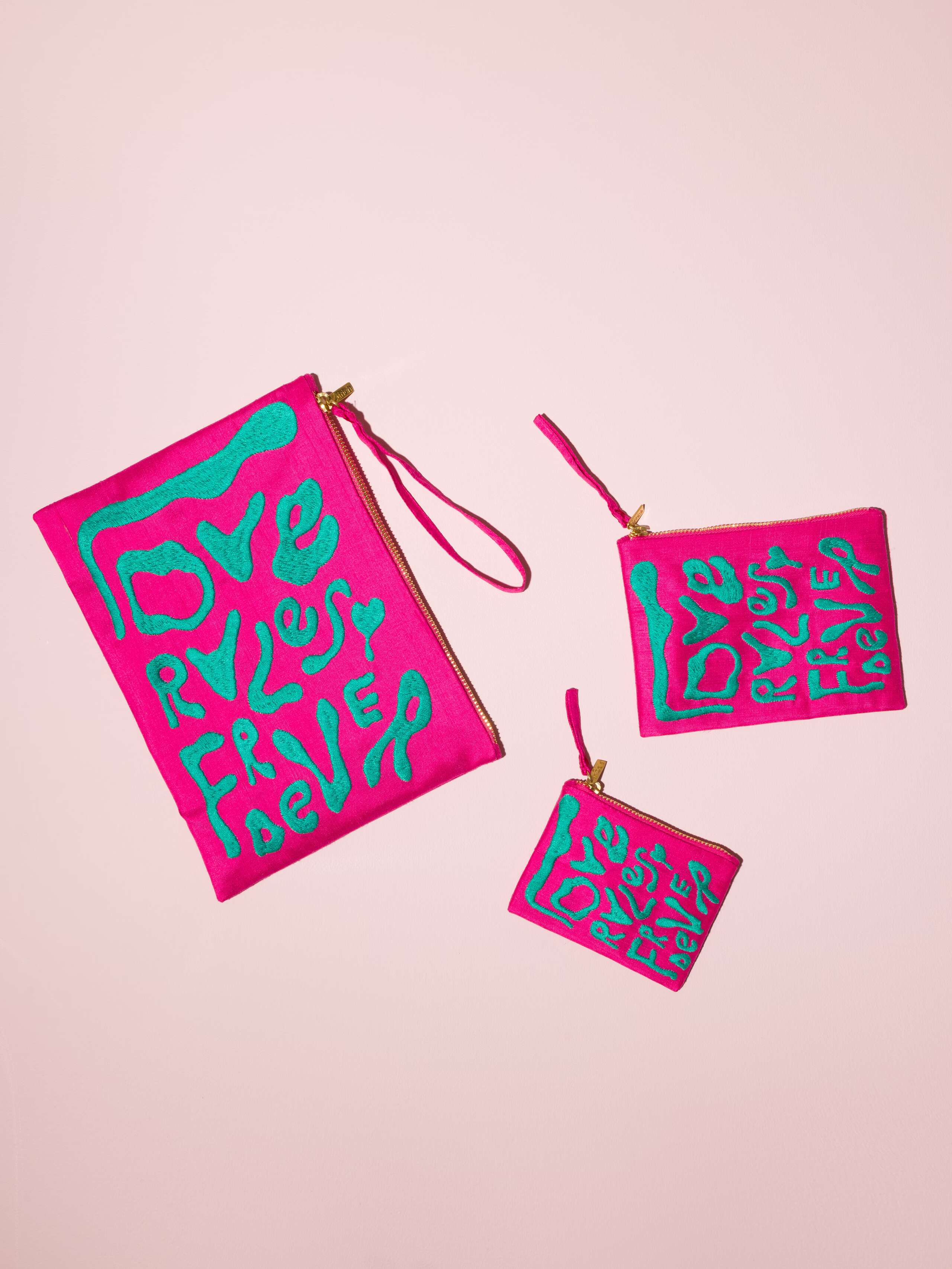 Picture of three pink silk clutches in three different sizes featuring the motto love rules forever