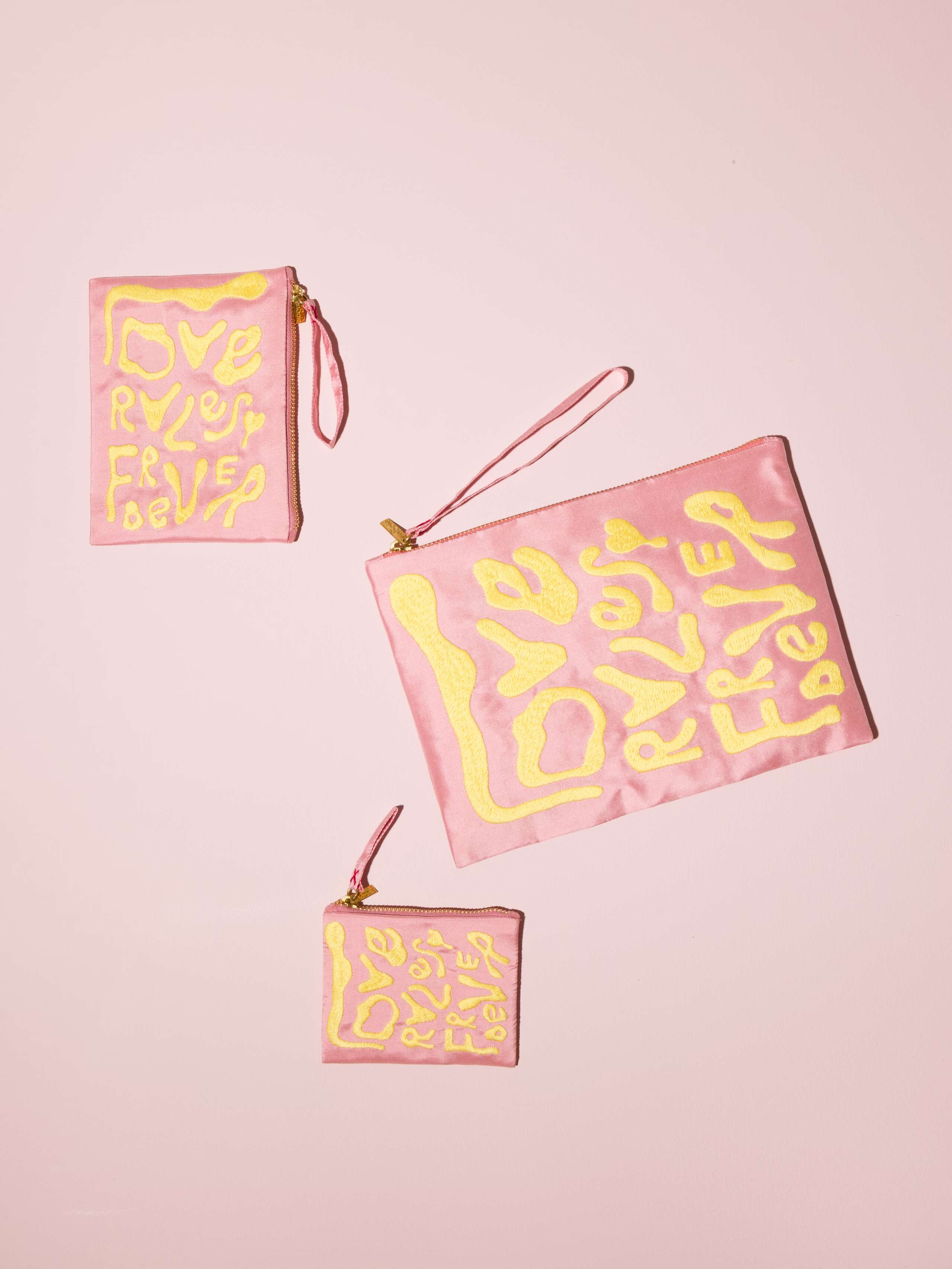 Picture of three blush pink silk clutches featuring the motto Love Rules Forever