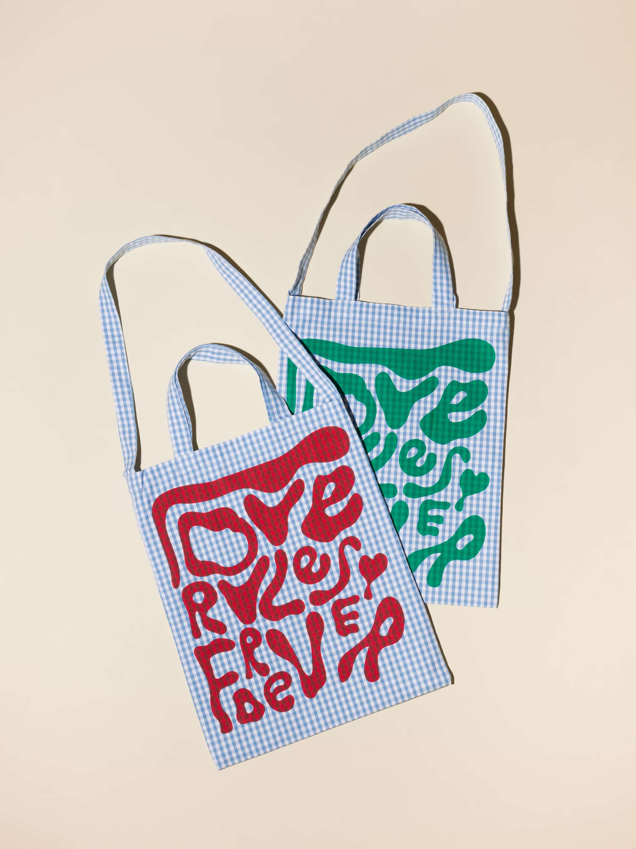 Picture of two light blue tote bags featuring the screen printed motto love rules forever
