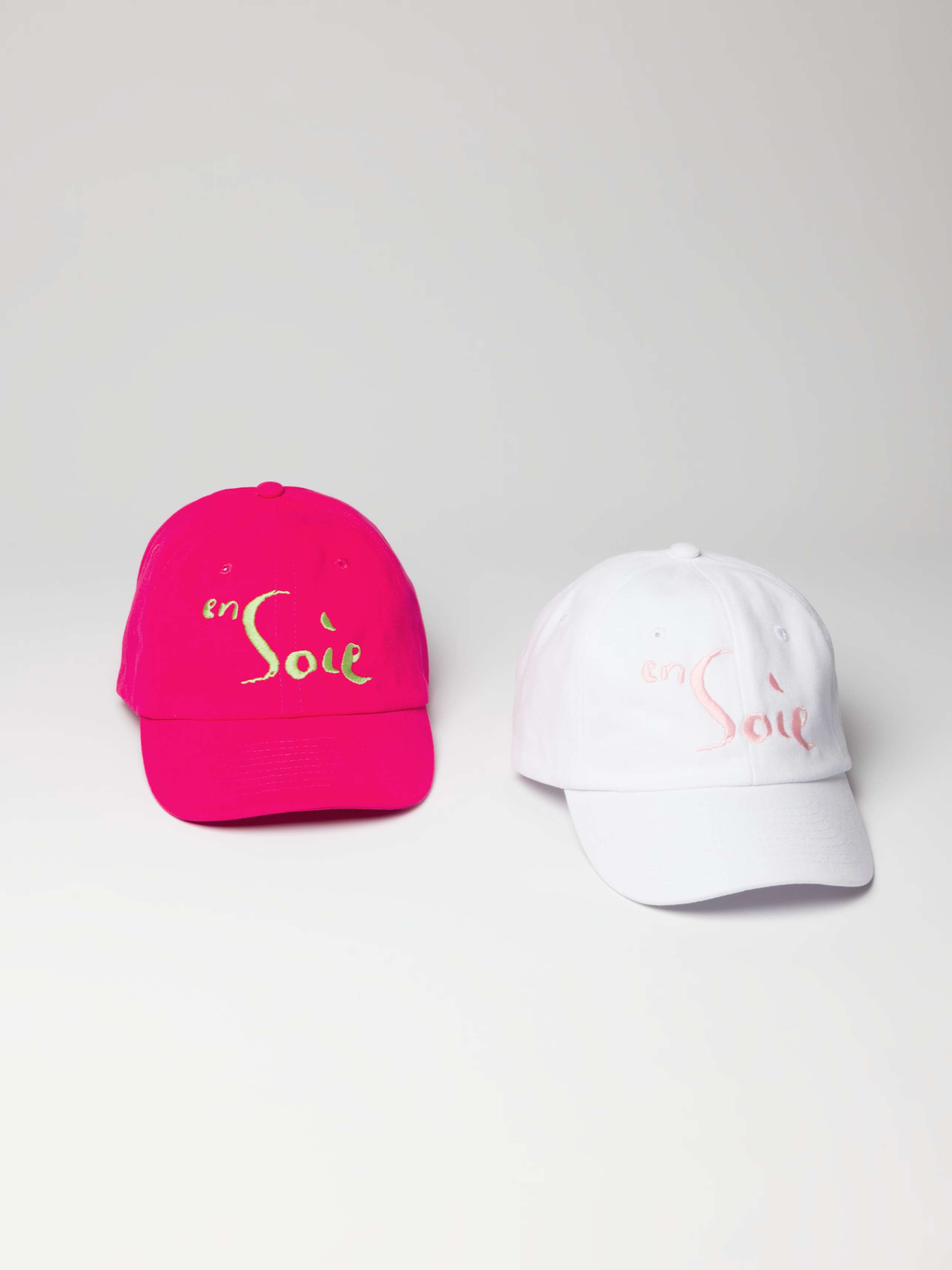 Picture of a pink and a white cap featuring an enSoie logo