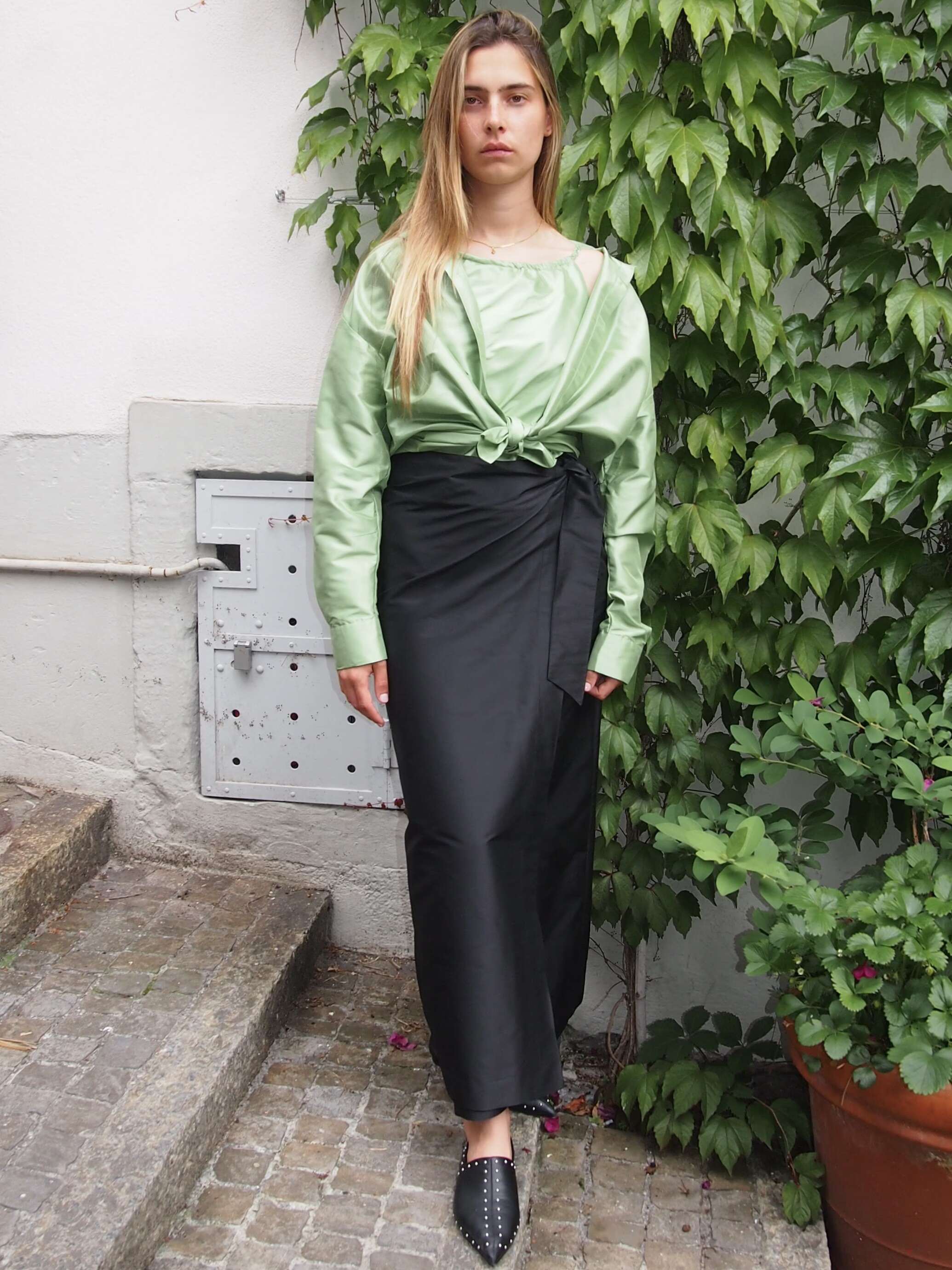 Model is wearing a green top in combination with a black long skirt