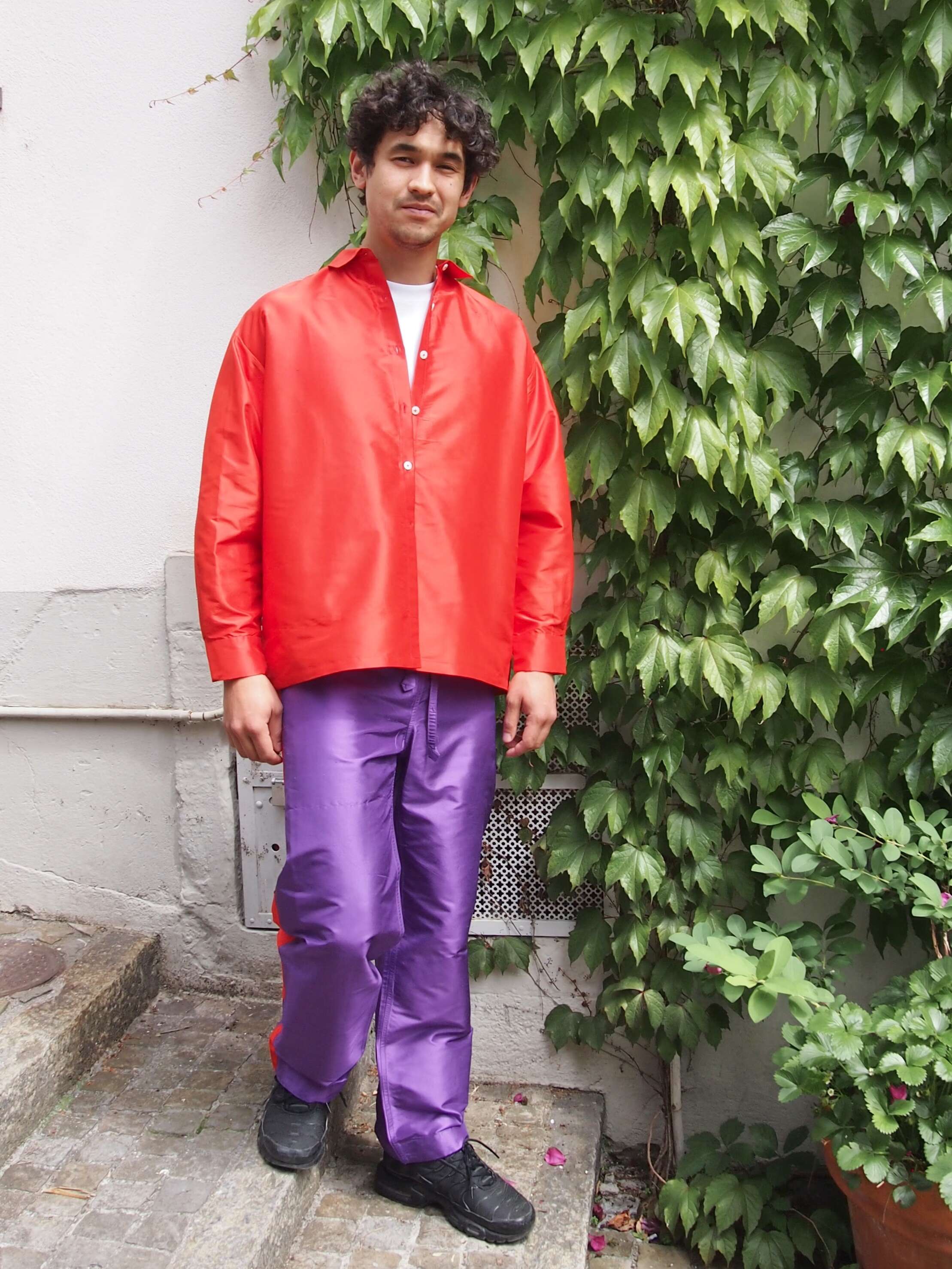 Picture of a male model wearing a purple silk trousers in combination with a red silk shirt