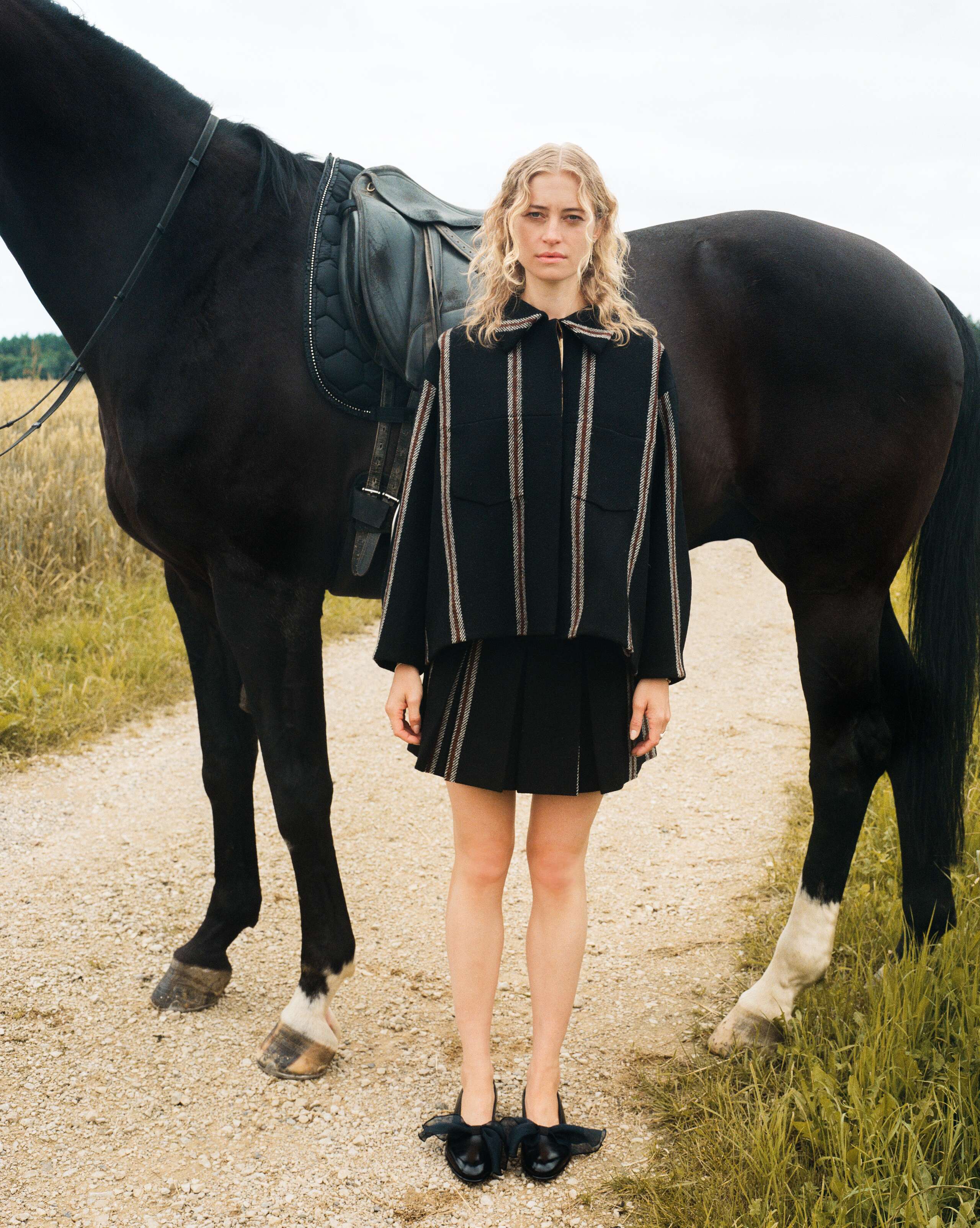Picture of a female model standing in front of a black horse wearing a skirt and jacket made from Harris Tweed
