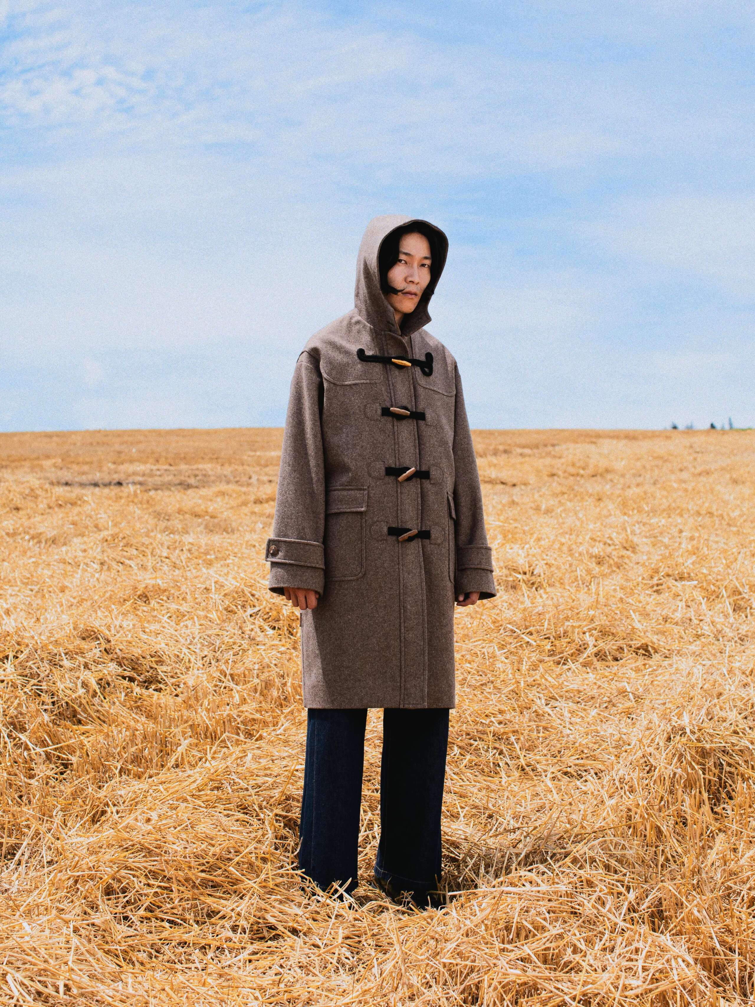Picture of a male model standing in a yellow corn field wearing a loden wool coat