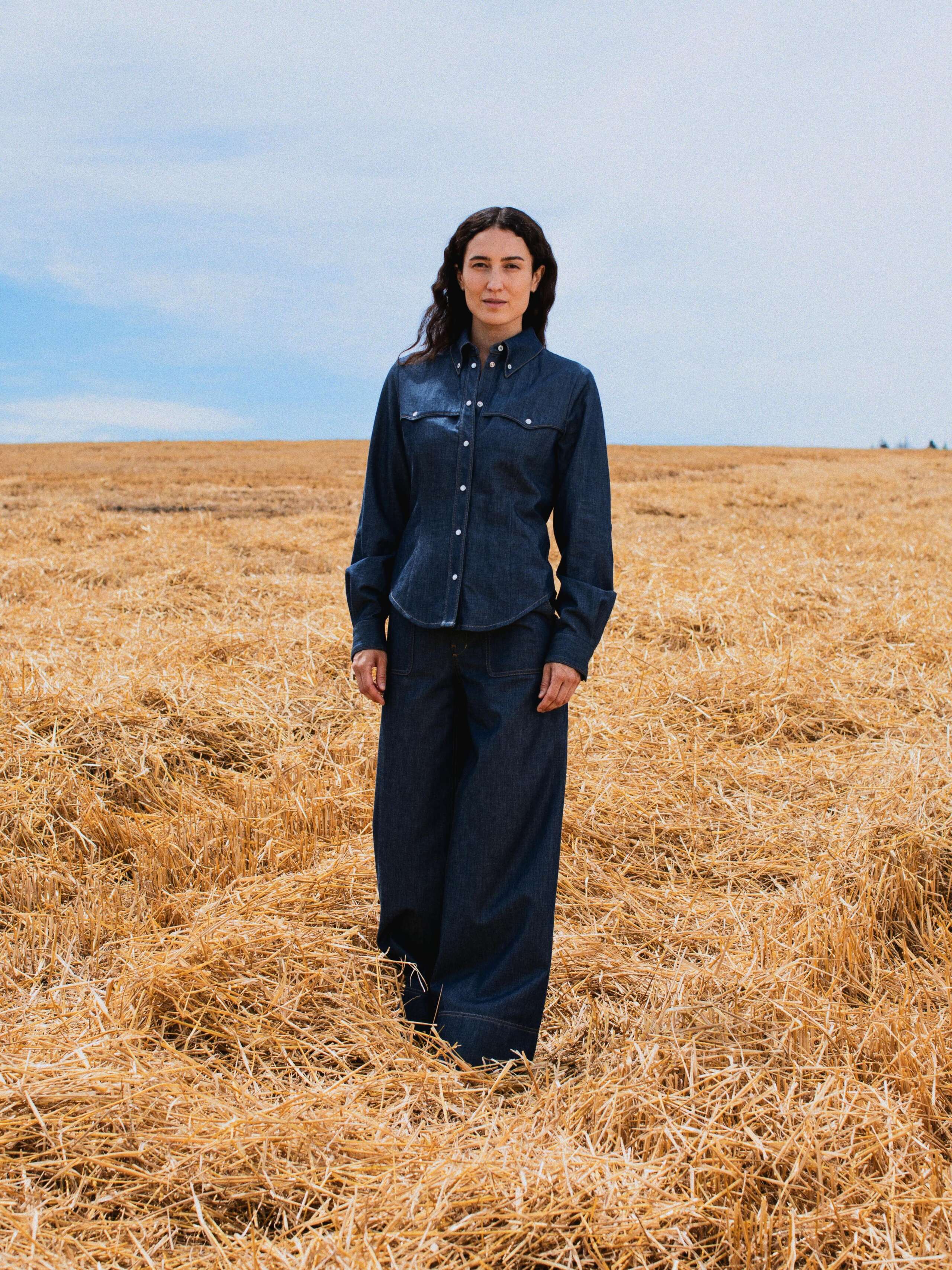 Picture of a female model standing in a yellow corn field wearing a denim blouse and a jeans