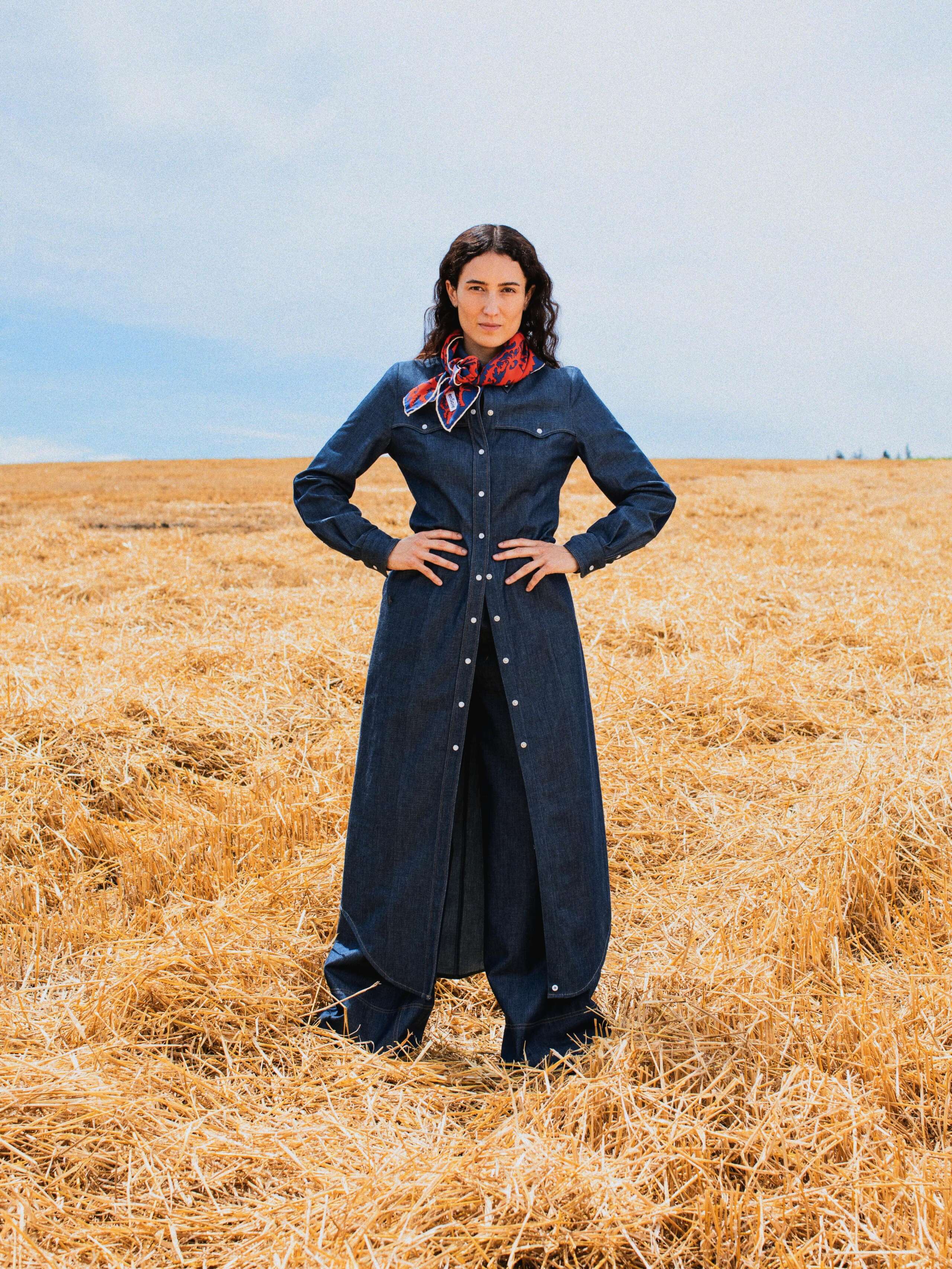 Picture of a female model standing in a yellow corn field wearing a denim blouse and a jeans