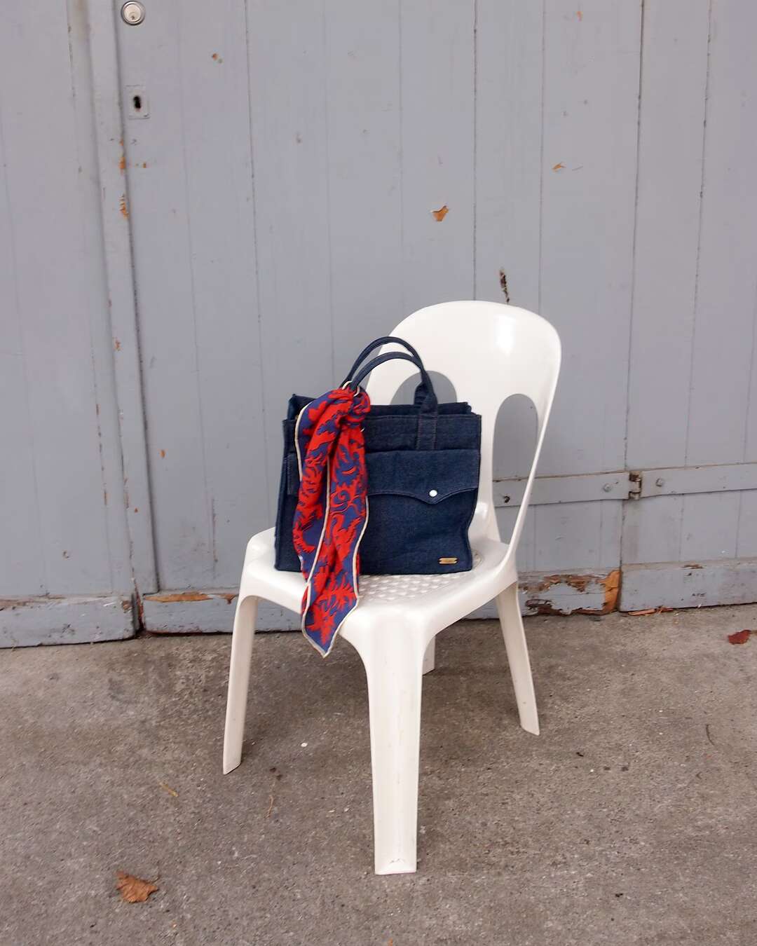 A white plastic chair with a denim bag on it