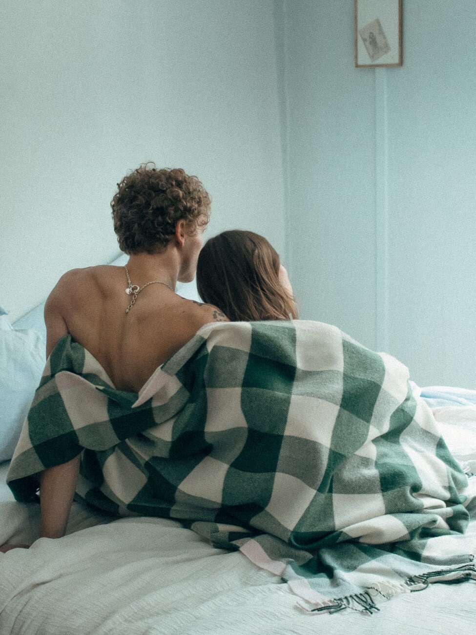 Picture of a couple sitting on a bed wrapped in a wool blanket 