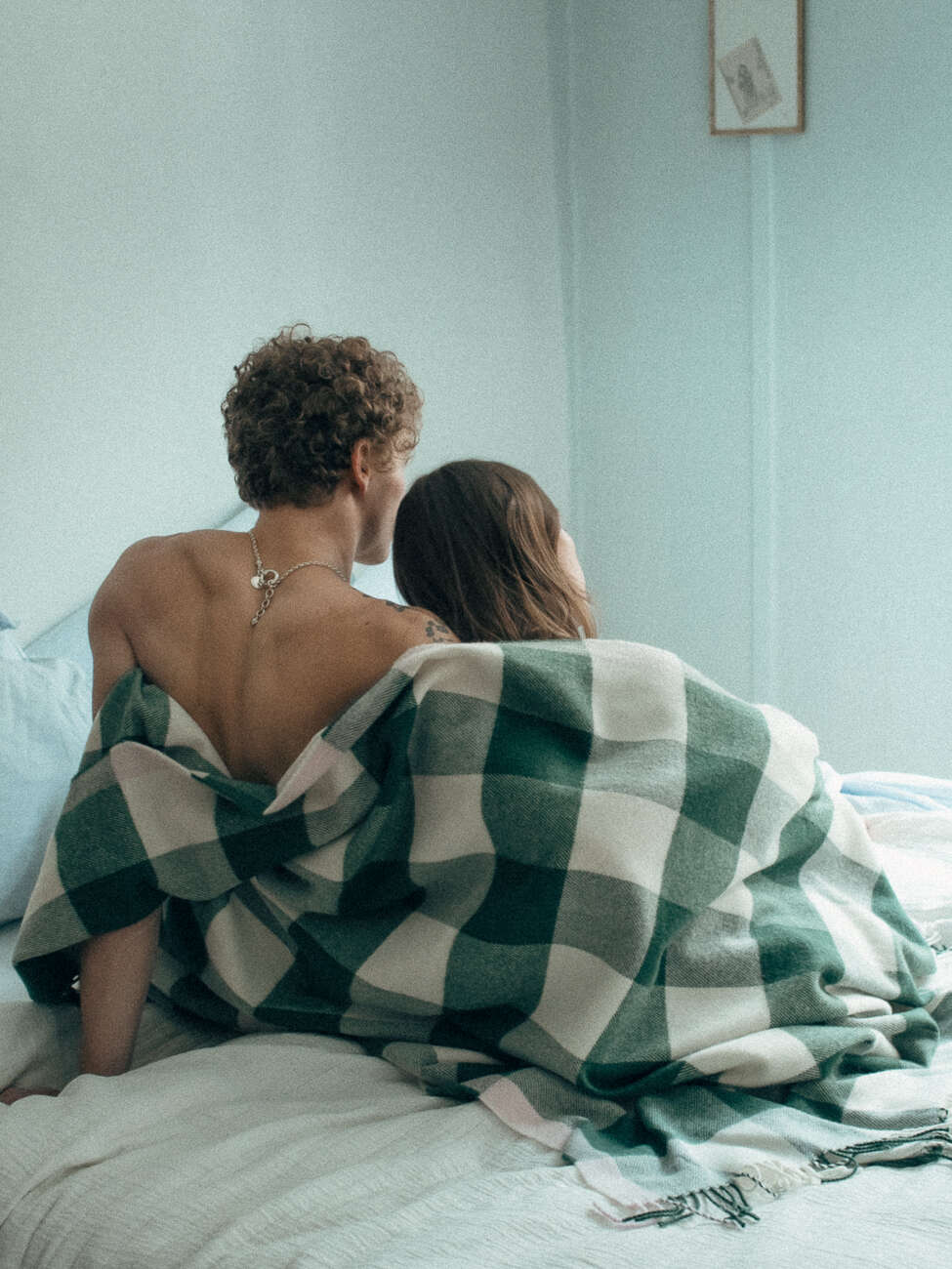 Picture of a couple sitting on a bed wrapped in a wool blanket 