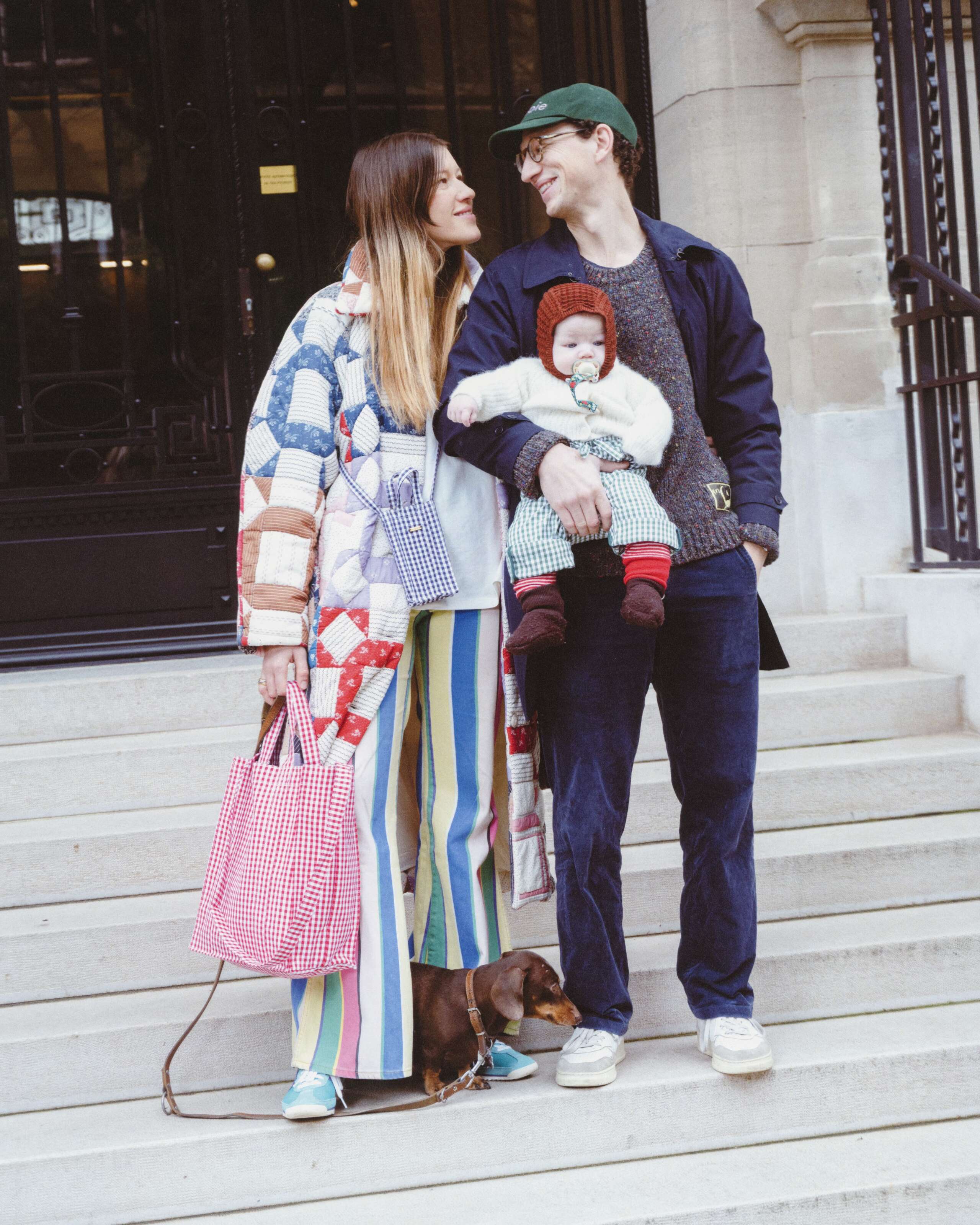 Picture of a couple with baby. They are colourfully dressed. He is wearing an enSoie cap. She carries a classic Cabas bag featuring a red vichy check pattern.