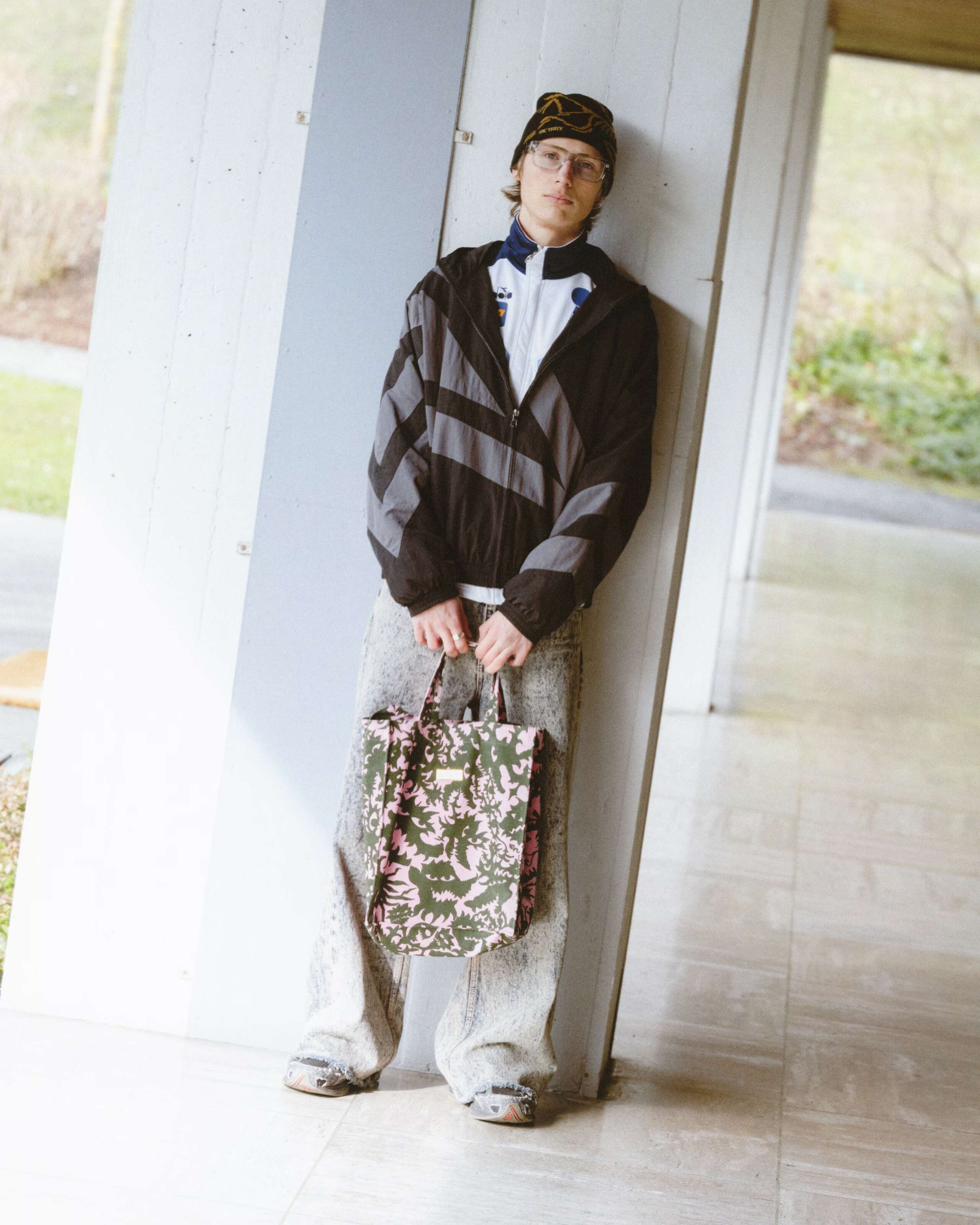 Picture of a young man wearing a grey jeans in combination with a grey trainer jacket.