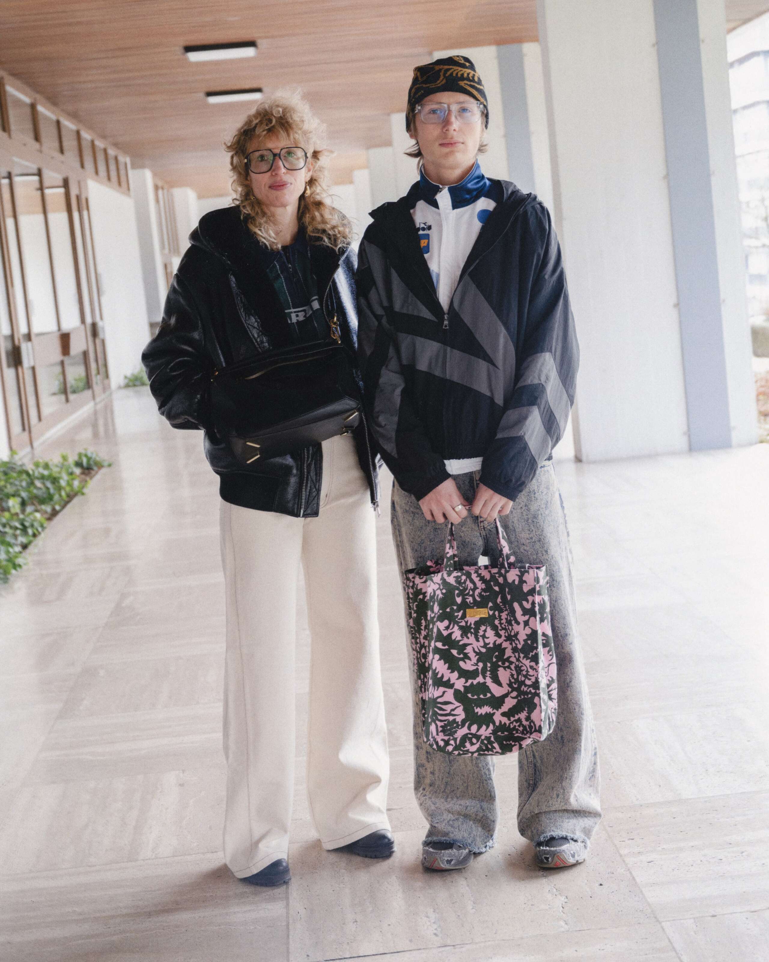 Picture of a women wearing white jeans and a black leather jacket and a young man wearing a grey jeans in combination with a grey trainer jacket.