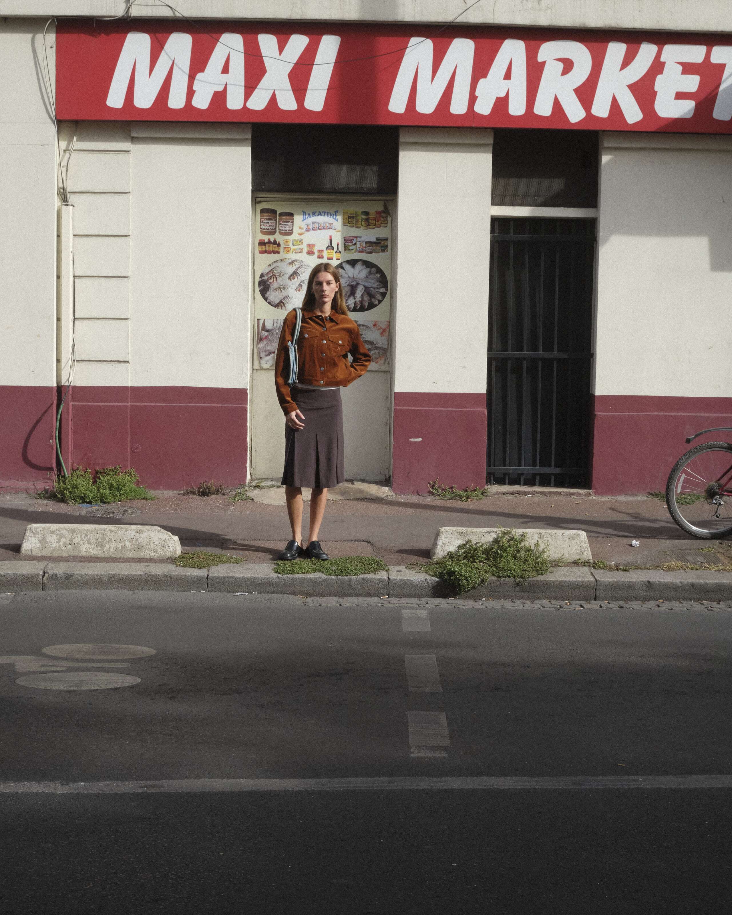 A young women is standing in front of a Maxi Market wearing the enSoie Jill jacket